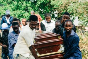 casket-africa-bunting-kargbo-2gAE2ItiMkw-unsplash(https-::unsplash.com:photos:a-group-of-people-standing-around-a-wooden-casket-2gAE2ItiMkw)