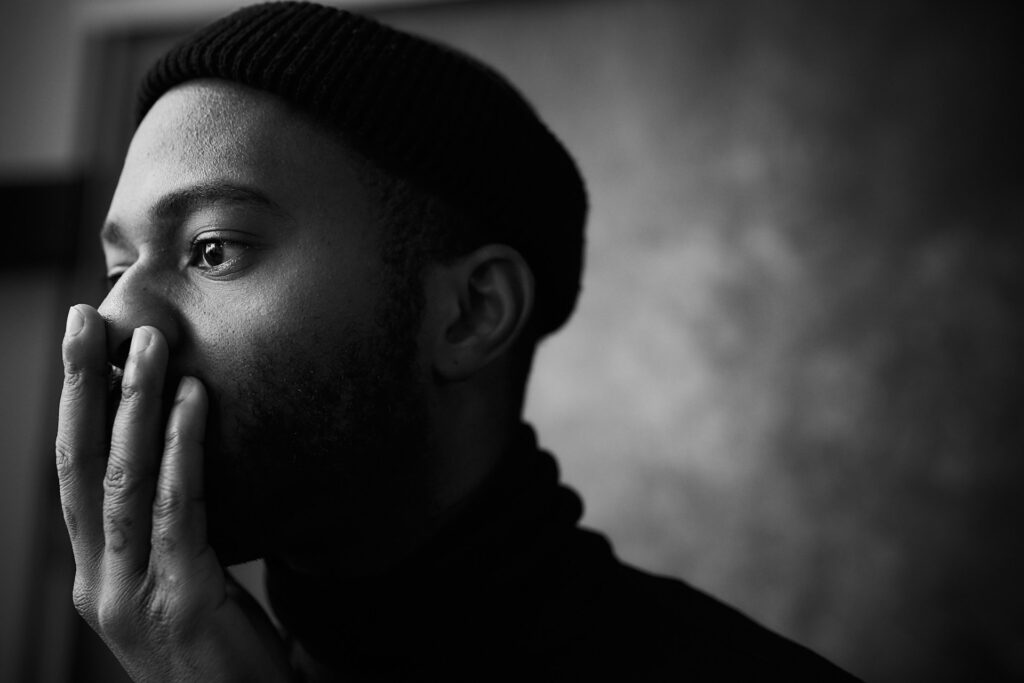young black man with hand over nose and mouth looking away to the left in distant thought symbolic of allowing doubt and unbelief in our minds