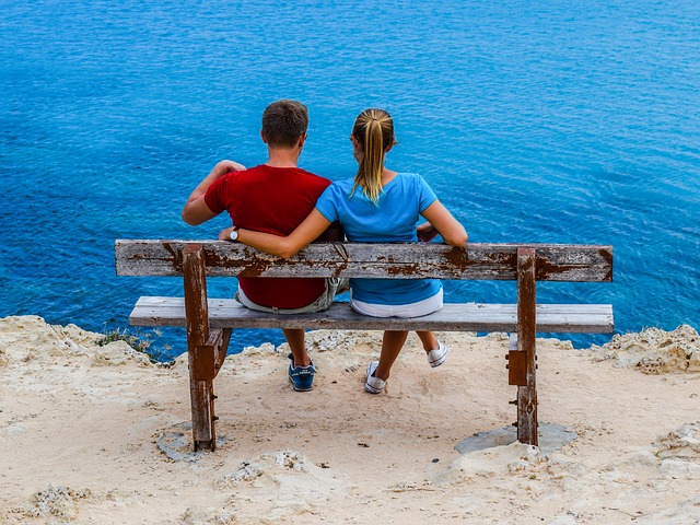 A young couple sitting on bench in a relationship while looking at a body of water.