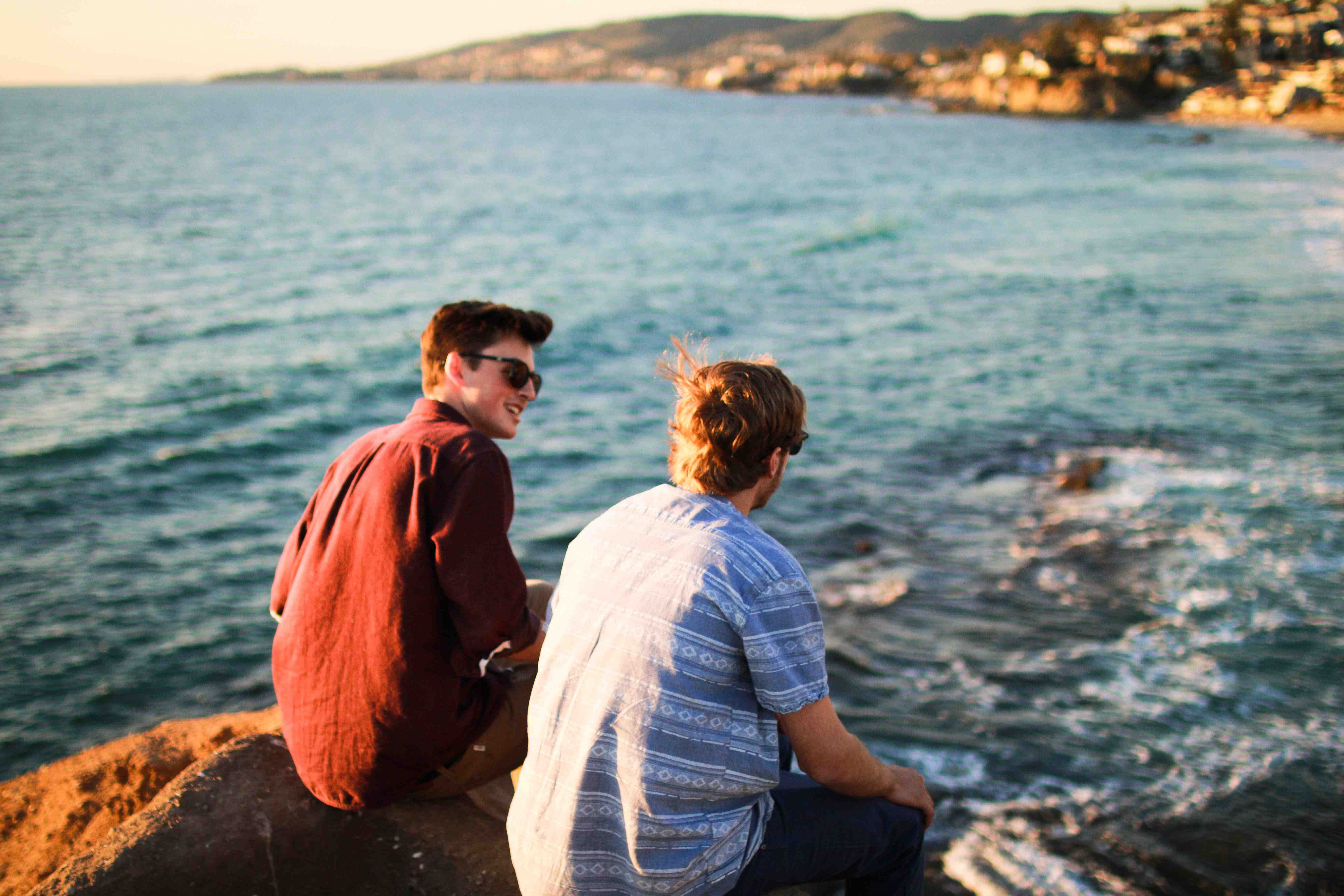 Two young men talking about their future while sitting on rocks overlooking a large body of water.
