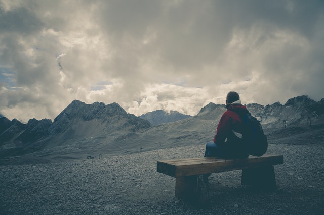 man sitting on bench with distant mountains