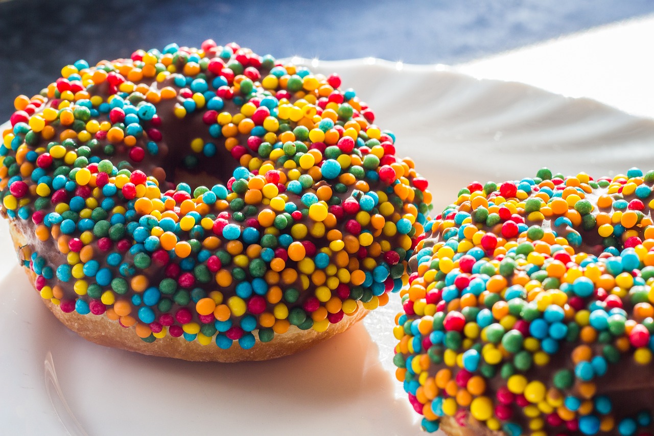 two well lit rainbow colored candy sprinkle coated donuts on a white plate