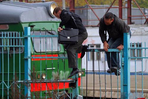 Two men taking a shortcut by climbing over a fence in a rail station
