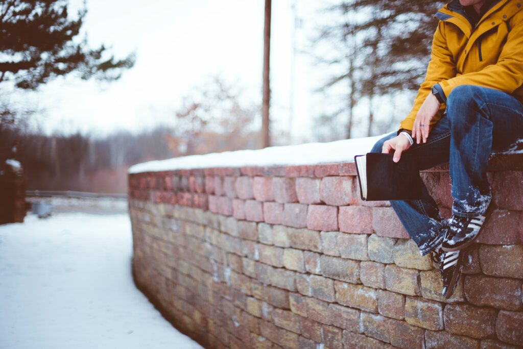 Cropped view of man sitting on snow covered wall holding Bible