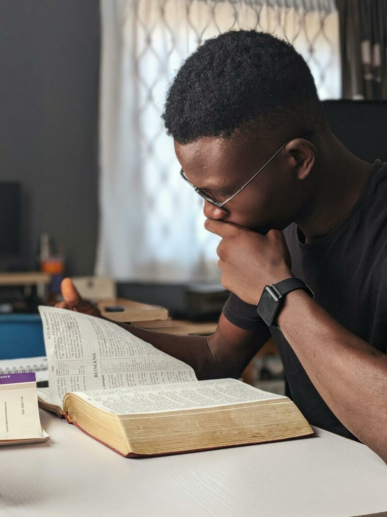 Man sitting in room while reading Bible resting on table