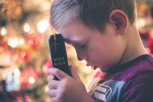 Boy with eyes closed holding Bible against bowed head