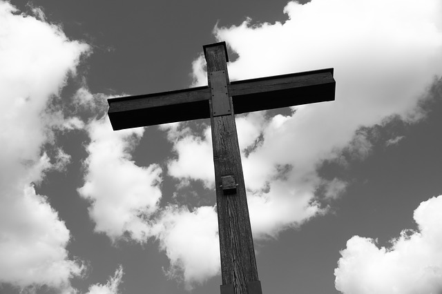 A black and white photo of an empty cross against a partly cloudy sky. A symbol of where the focus of our faith should be.