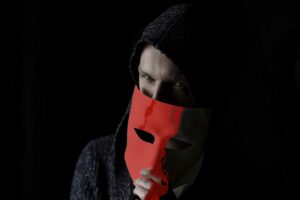 Man in dark hoodie removing red devil mask