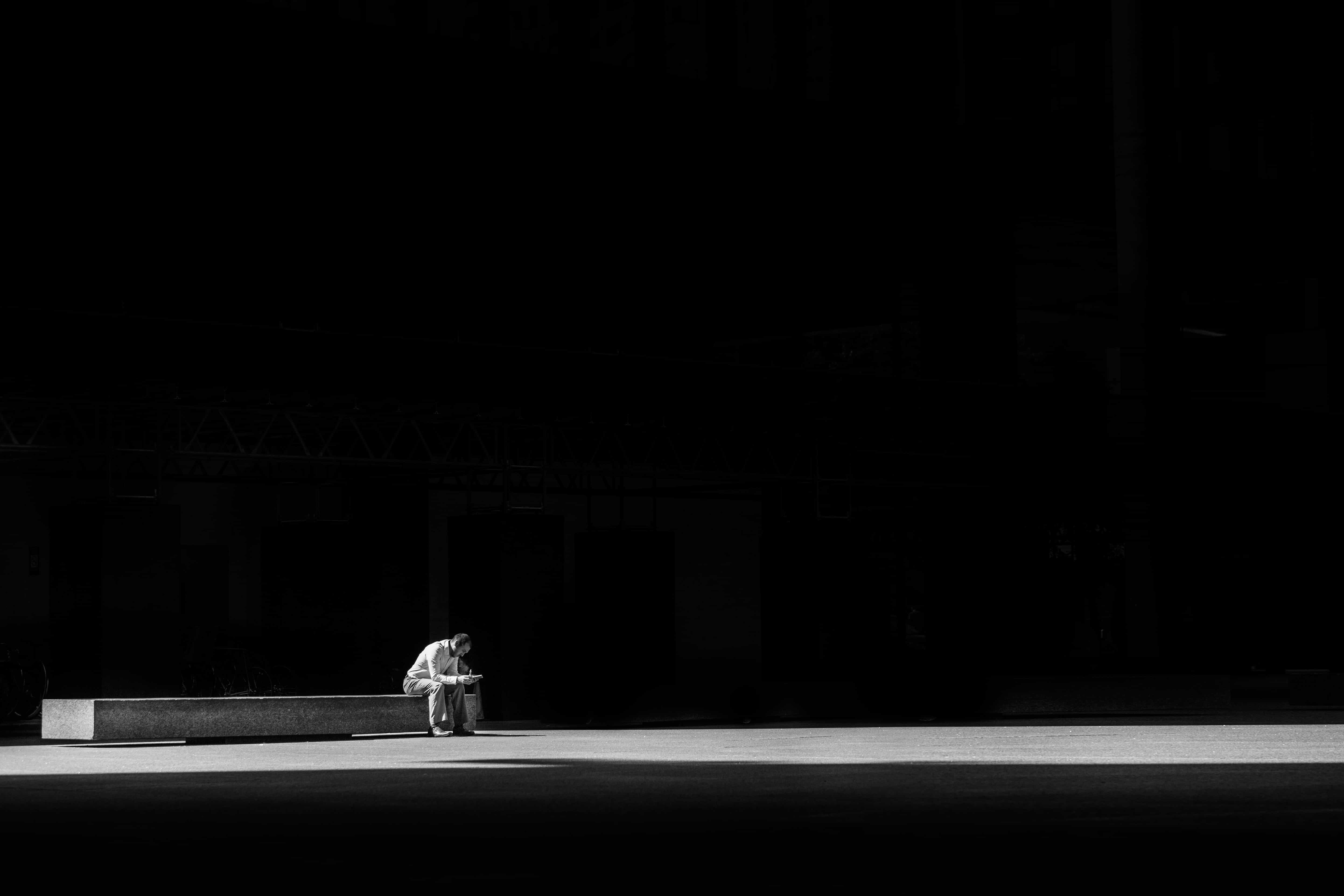 Man sitting alone in large area with dark background in sunlight