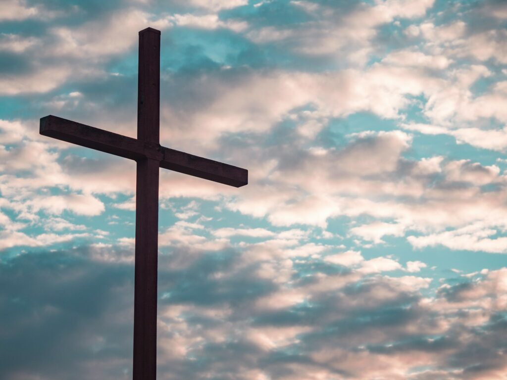 A silhouette of wooden cross against a cloudy blue sky. Symbolic of the one was born to die