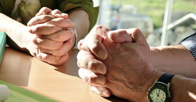 Two pairs of sunlit folded hands resting on on a table outdoors