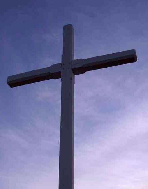 a picture of a wooden cross with a partly cloudy sky behind at sunset