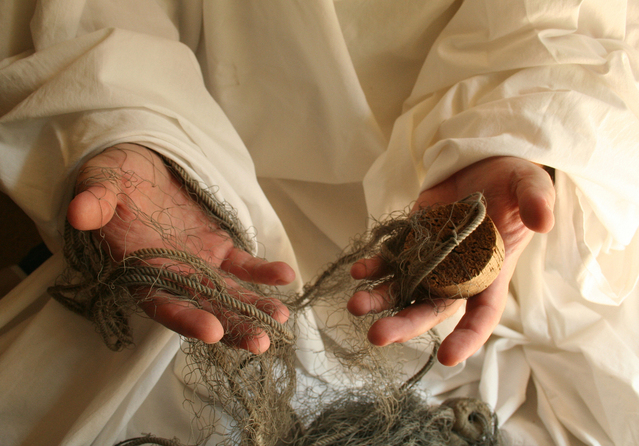 A man in linen garment holding a portion of fishing net in hands