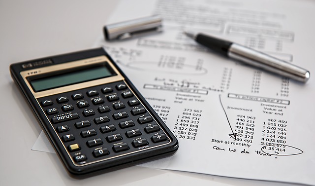 calculator, open pen and paper with financial figures laying on flat white surface