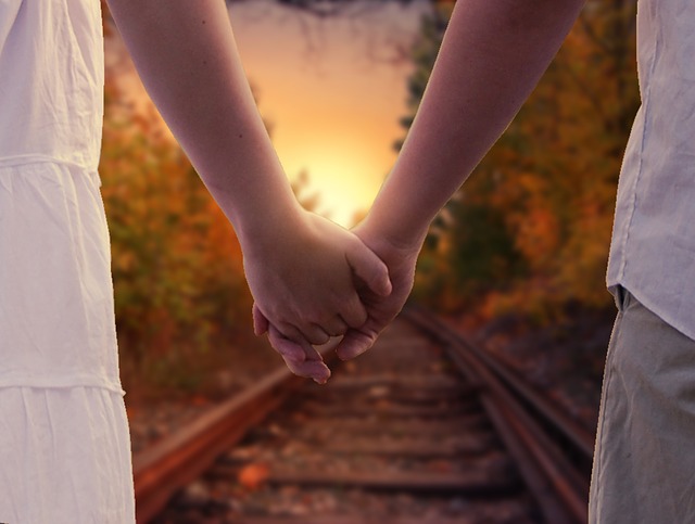 young couple holding hands while walking down a railroad track symbolic of holding God's hand
