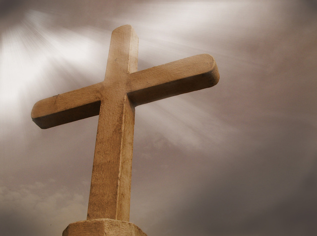 brown concrete cross with light beams shining through thick grey clouds