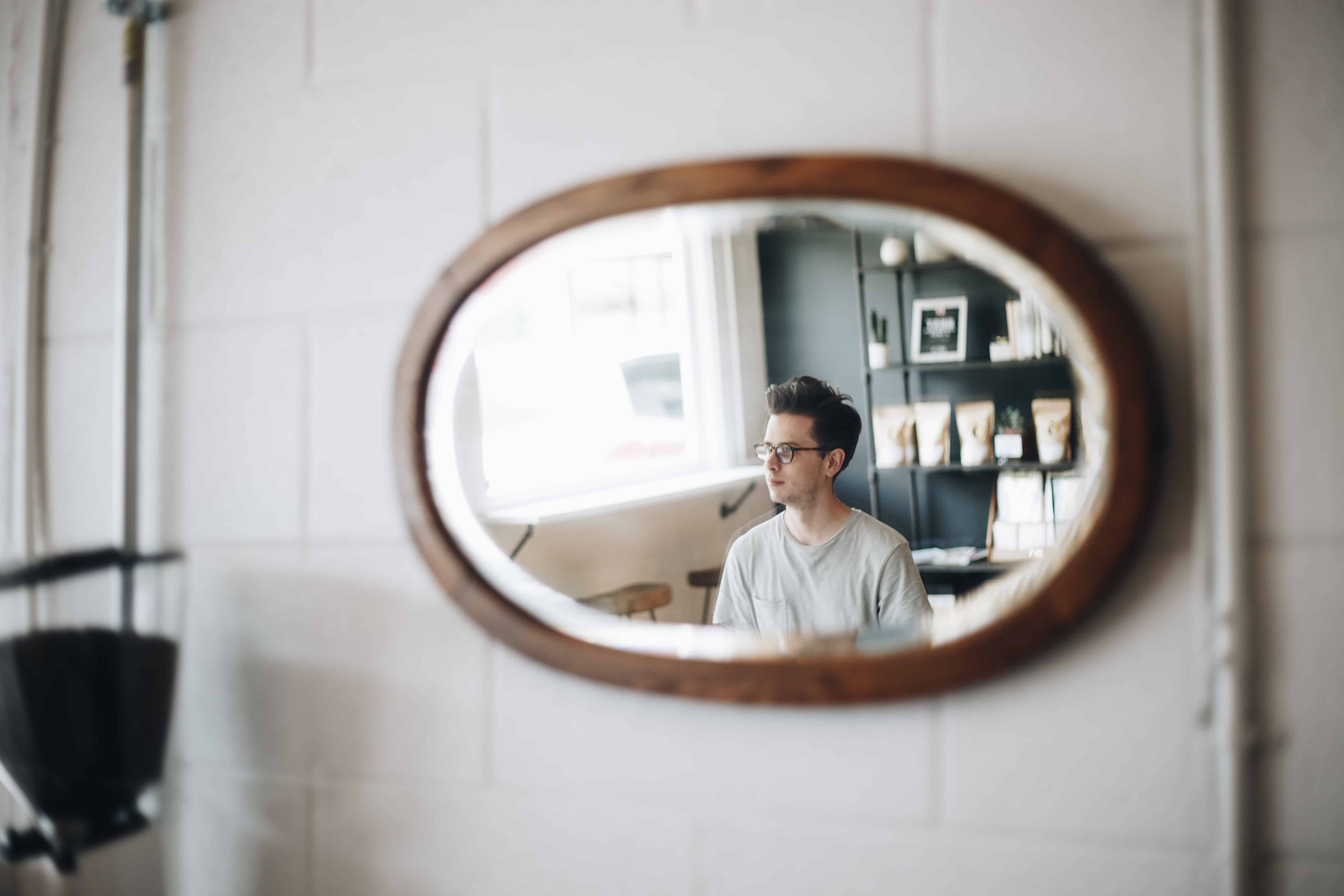 image of seated man with glasses in mirror hanging on tiled wall