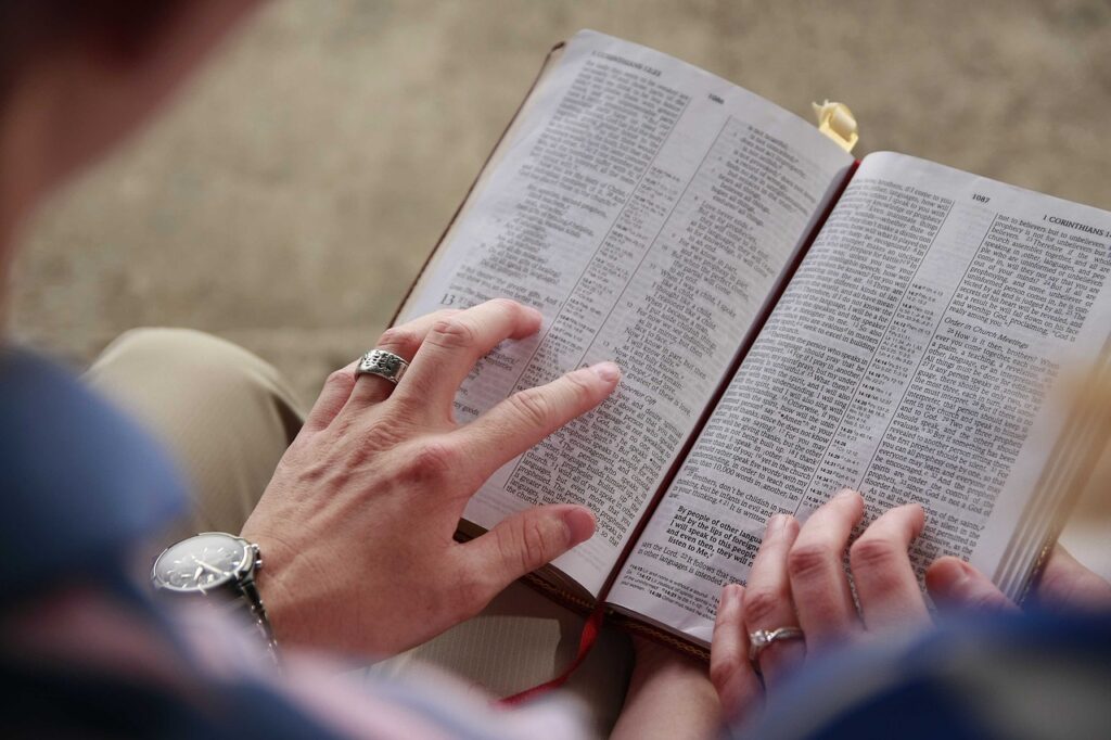 A person hands resting on an open Bible in their lap symbolizing of one searching about what God means