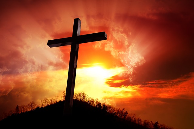 photo of a cross on a hill with sun, clouds and red sky in background