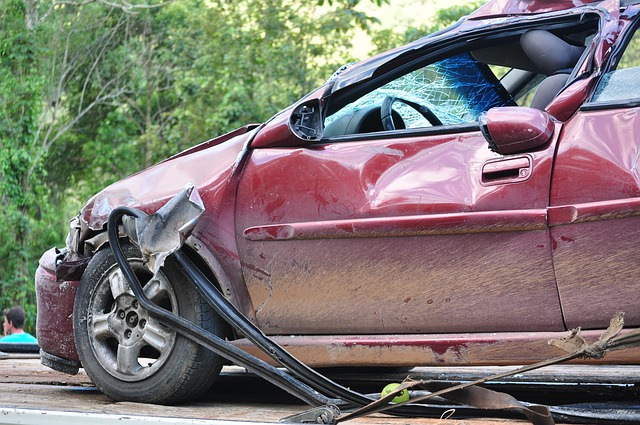 A photo of the side view of a small red car that was involved in an accident.