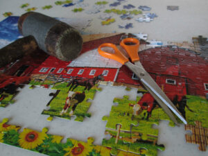 A photo of a puzzle containing several incorrectly placed pieces with a mallet and scissors resting on top