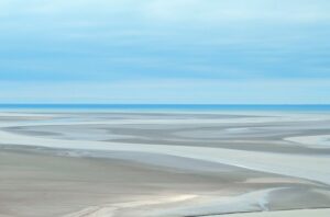 shallow water winding though sand with a large body of water in the background