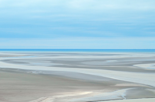 shallow water winding though sand with a large body of water in the background