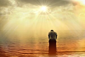 photo of man bowing slightly in water with sun, clouds and sunbeams above him
