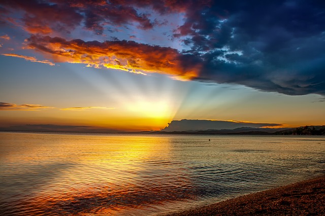 photo of sunset behind clouds over water with sunbeams highlighting clouds above and water below