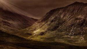 A photo of a green valley in between darkened mountains with beam of sunlight highlighting a portion of the valley