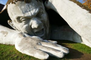 A very large stone sculpture of a giant man trying to climb out of the ground