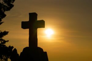 cross silhouette with yellow-orange sun with haze behind it