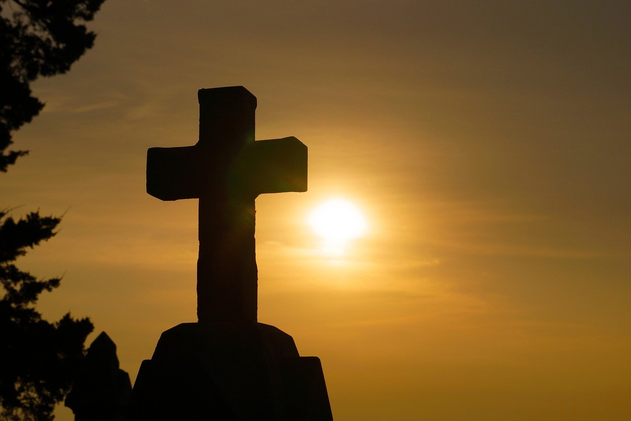 cross silhouette with yellow-orange sun with haze behind it