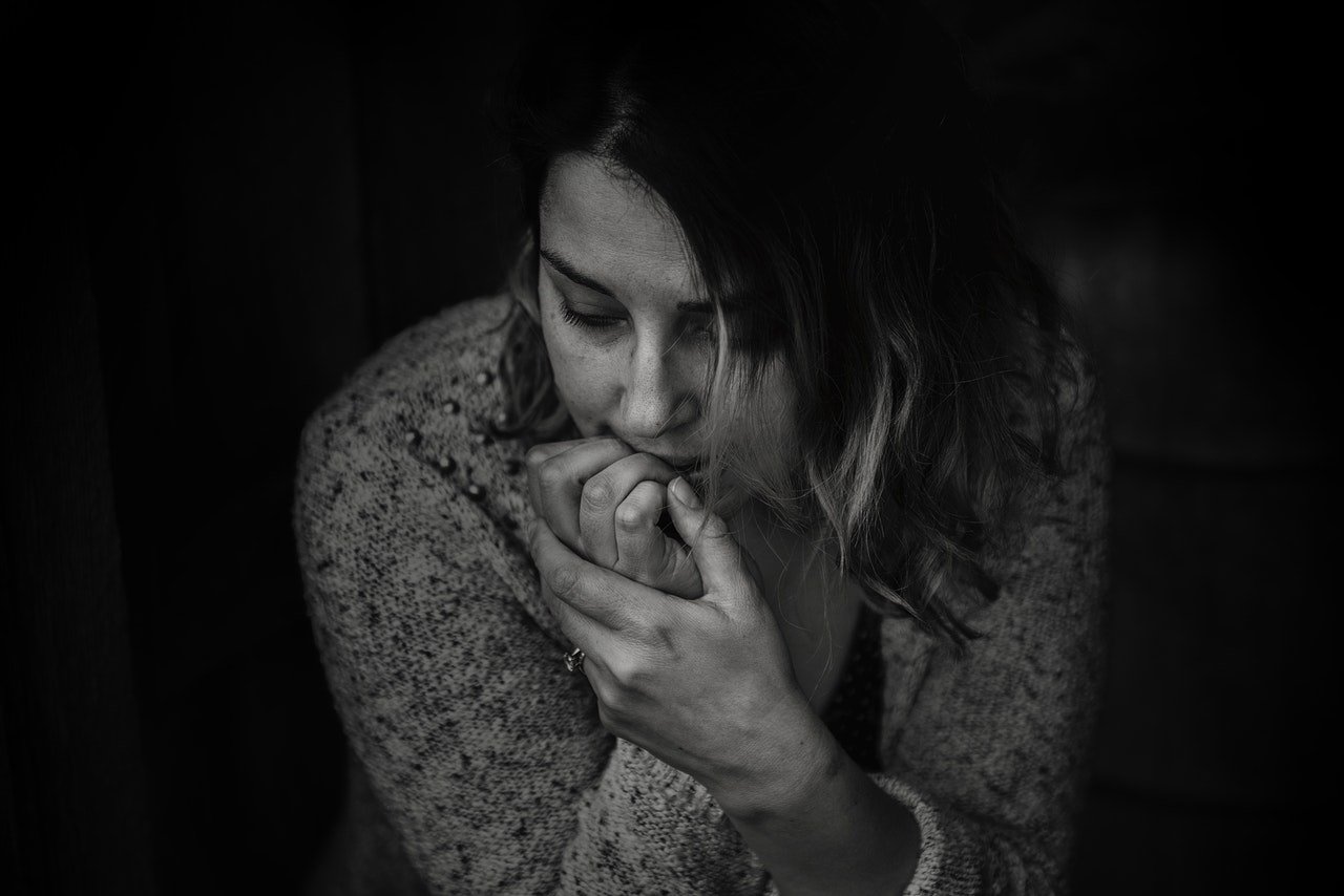 black and white picture of a woman leaning over with fingers of right hand in mouth with a worried or depressed expression