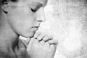 Black and white photo of woman with eyes closed and hands folded in prayer