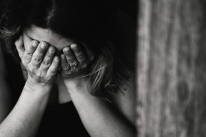 A black and white photo of a woman with head down in hands with the appearance of grief or sadness