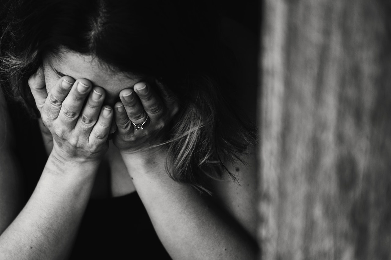 A black and white photo of a woman with head down in hands with the appearance of grief or sadness