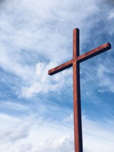 A large red wood cross against a clouded blue sky