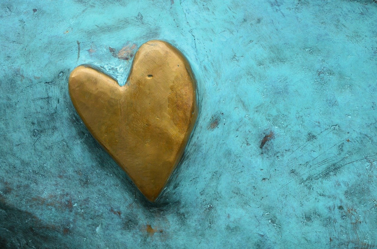 A raised gold painted heart on a turquoise painted stone surface