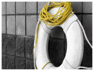 A white life preserver with coil of yellow rope hanging on a black stone tiled wall