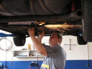 A mechanic grinding metal on the underside of a vehicle while it is raised inside of a garage