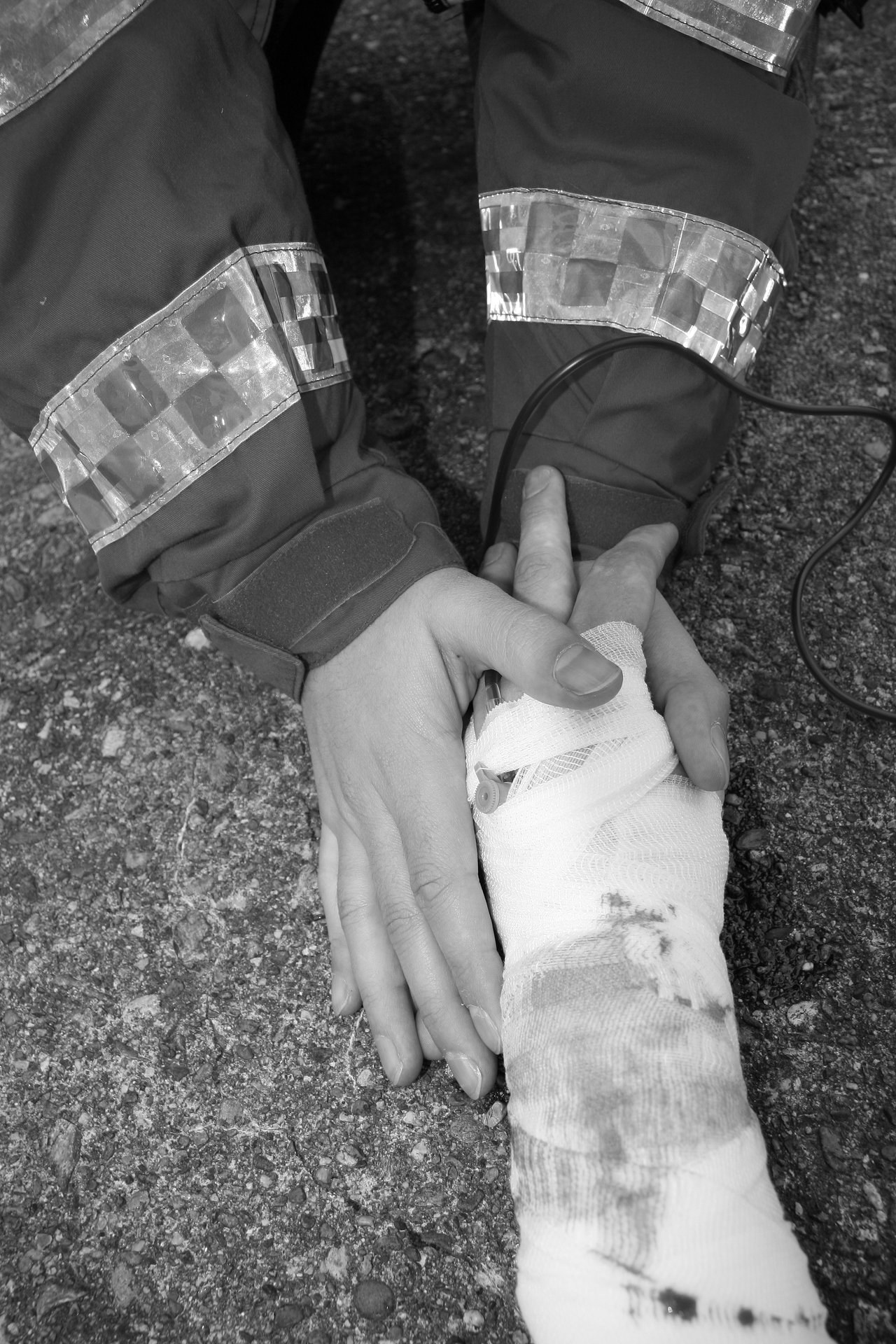 A black and white picture of the hands of a medic holding the bandaged hand of an injured person. An example of one who will go out of the way to help another.