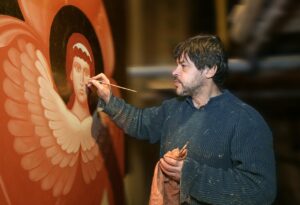 A man painting an angel with various shades of dark orange paint inside a large studio