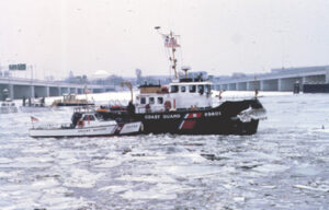 A photograph of the US Coast Guard cutter Capstan in the broken ice filled Potomac River near the 14th Street bridge in Washington, DC on a cloudy day