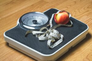 A scale on wooden floor with a tape measure and a piece of fruit on top