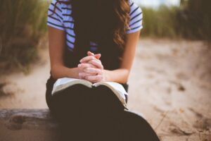 A photo of a woman seated with head down, hands folded on an open Bible
