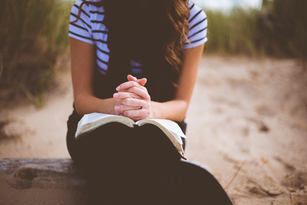 A photo of a woman seated with head down, hands folded on an open Bible