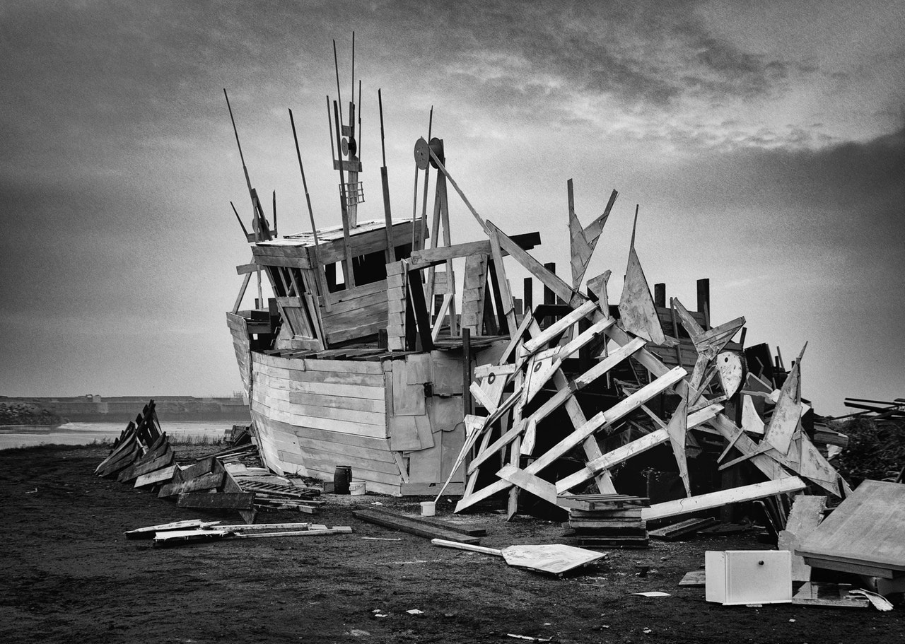 A black and white picture of a completely wrecked wooden fishing vessel on shore