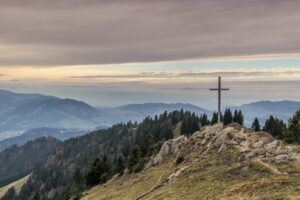 A cross on a rocky hillside in Austria with mountains in the distance and a cloudy pastel sky in the background