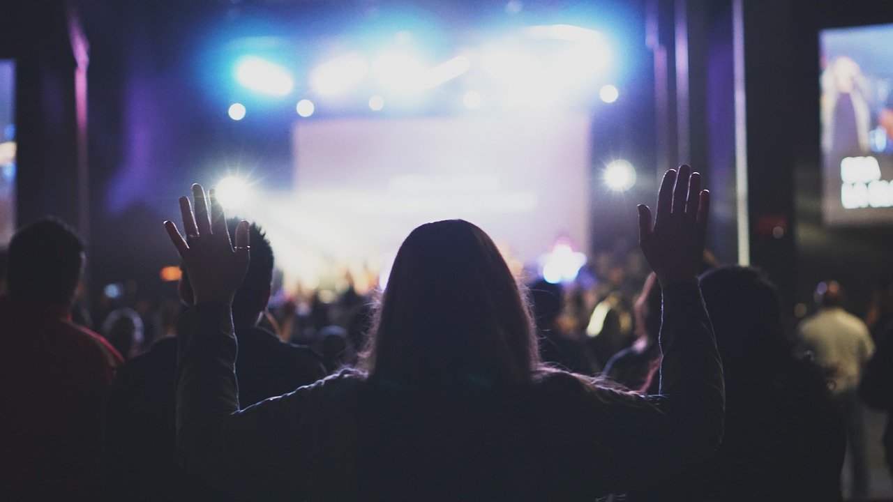 Silhouette of the backside of a younger female with both arms raised in stage lit church auditorium